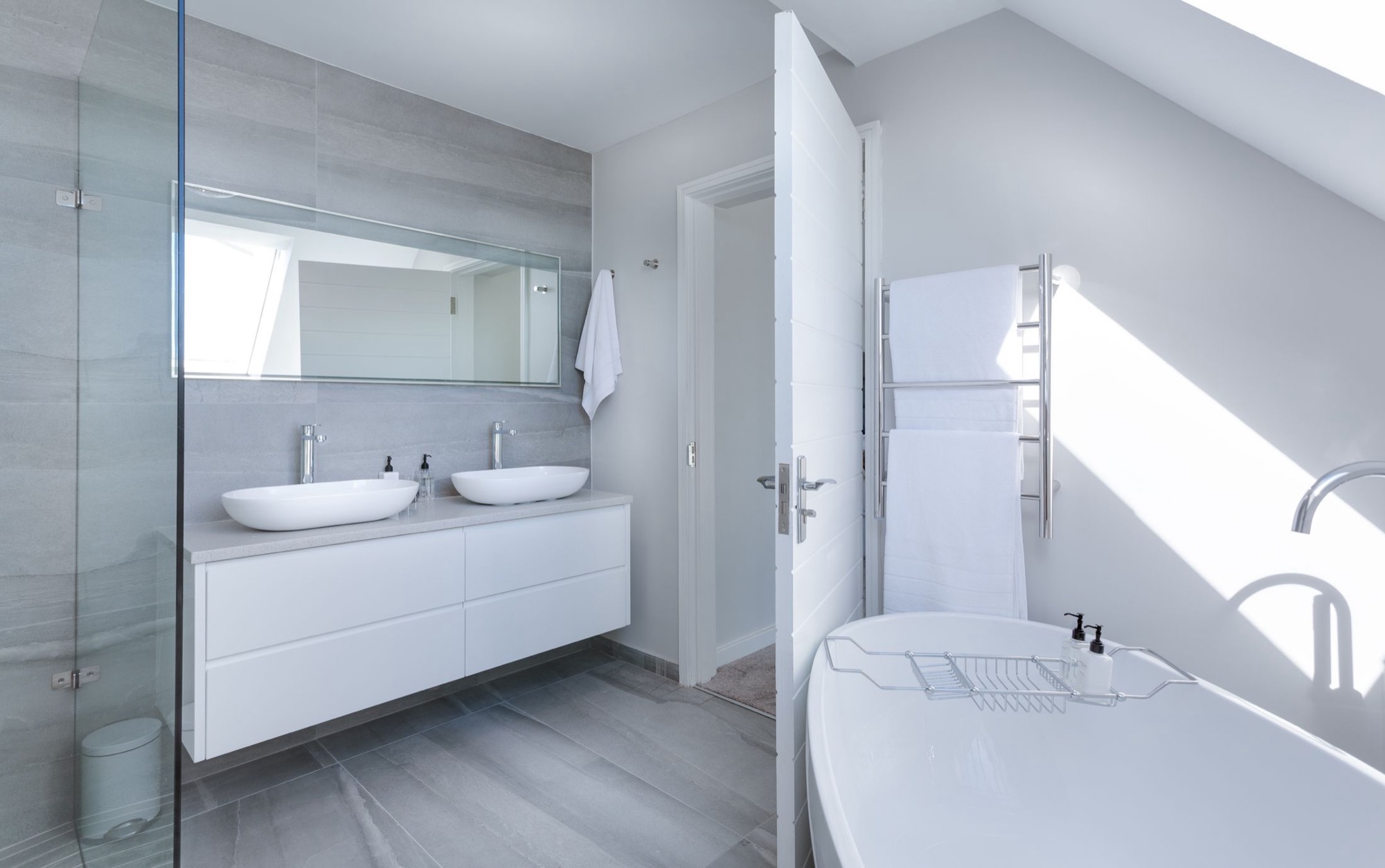 A bright modern bathroom with twin basins, a vanity unit and a glazed shower